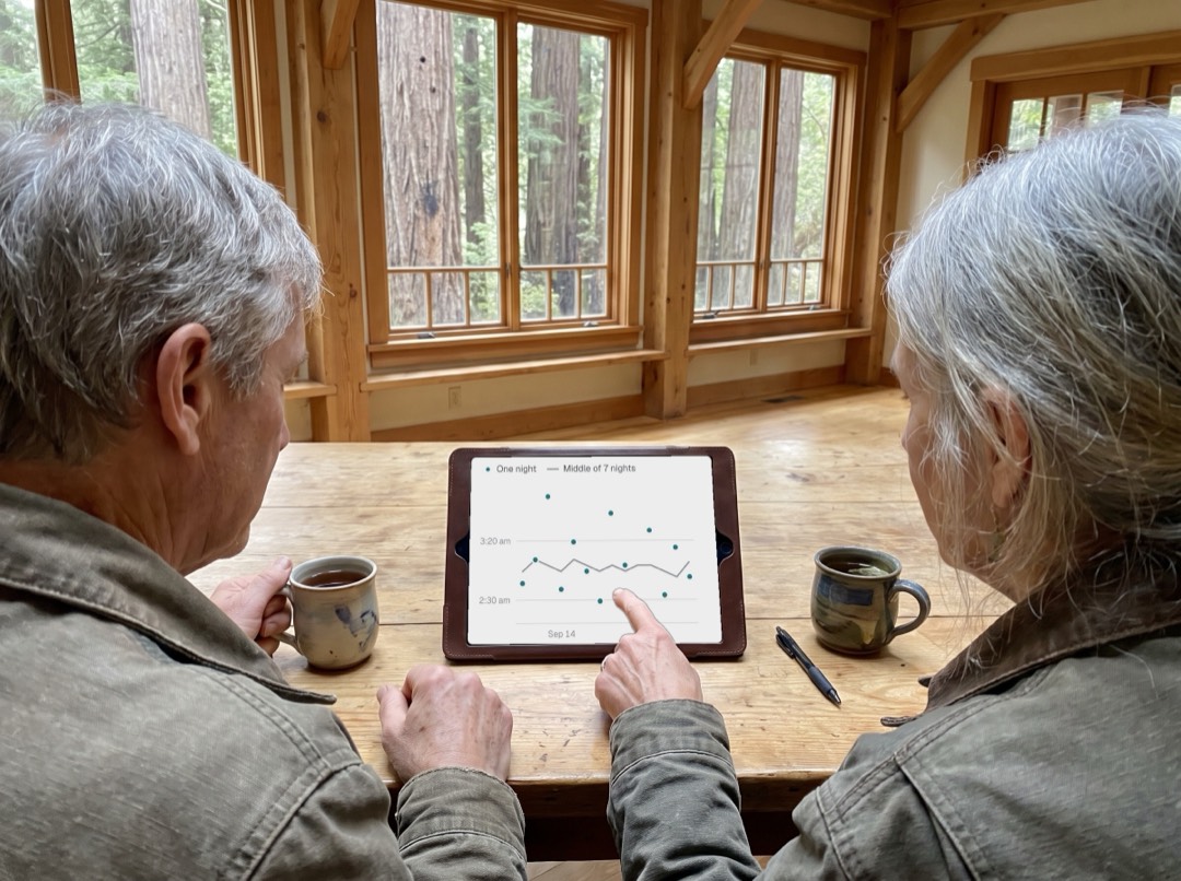 Two guests at a wooden table looking at a tablet that shows the middle of each night over two weeks
